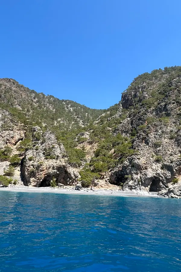 View of Kalogeros village nestled along a dramatic coastline with clear Aegean waters and scrubland cliffs.