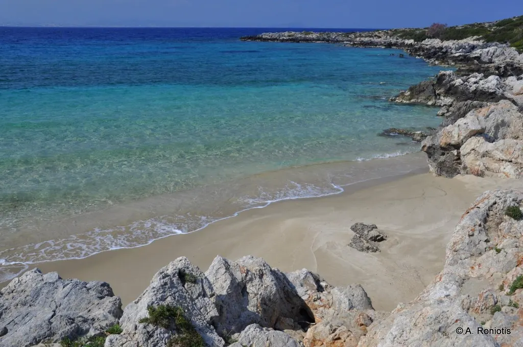Coastal view of Macherida showing clear azure waters and a small secluded beach nestled against rugged cliffs.