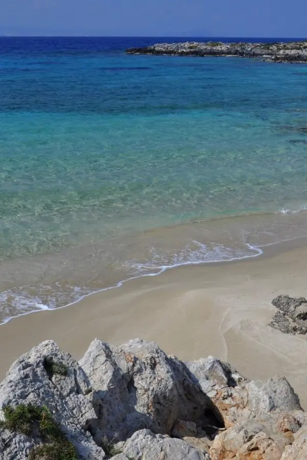 Coastal view of Macherida showing clear azure waters and a small secluded beach nestled against rugged cliffs.